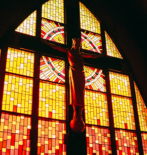 Christ on the cross with a stain glass window behind it