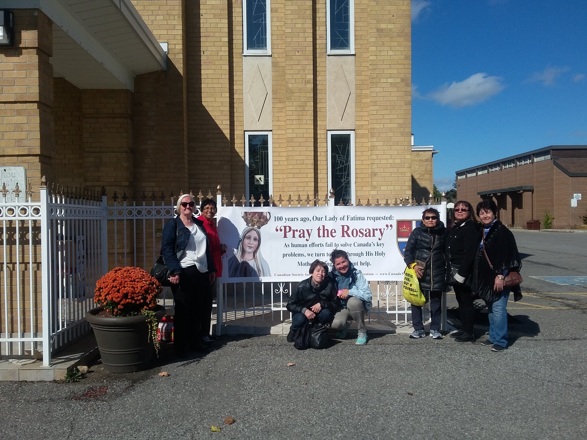 a few parishioners in front of rosary rally banner